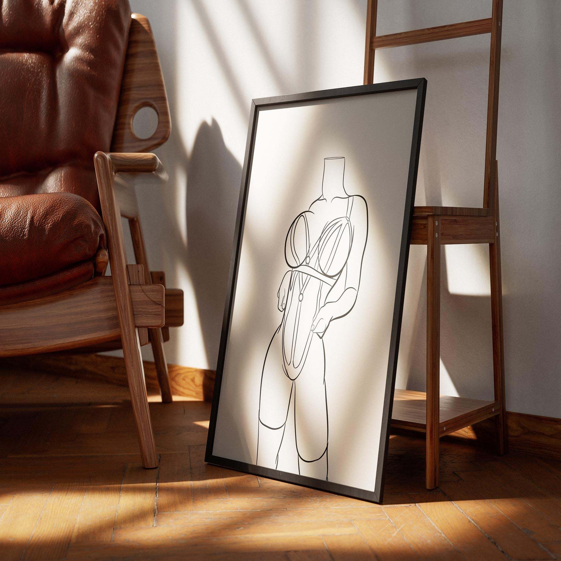 Line art illustration titled "Lingerie Model 62" in a framed print on a wooden floor near a chair.
